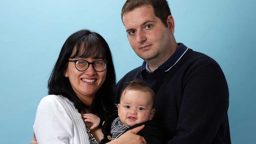 A man and woman stand in a family tableau holding a baby.