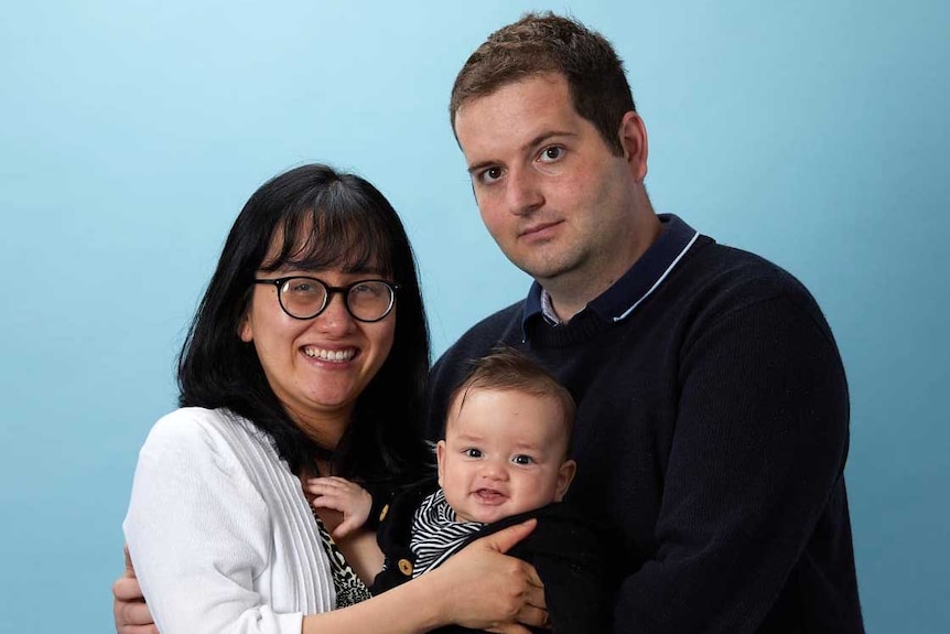 A man and woman stand in a family tableau holding a baby.