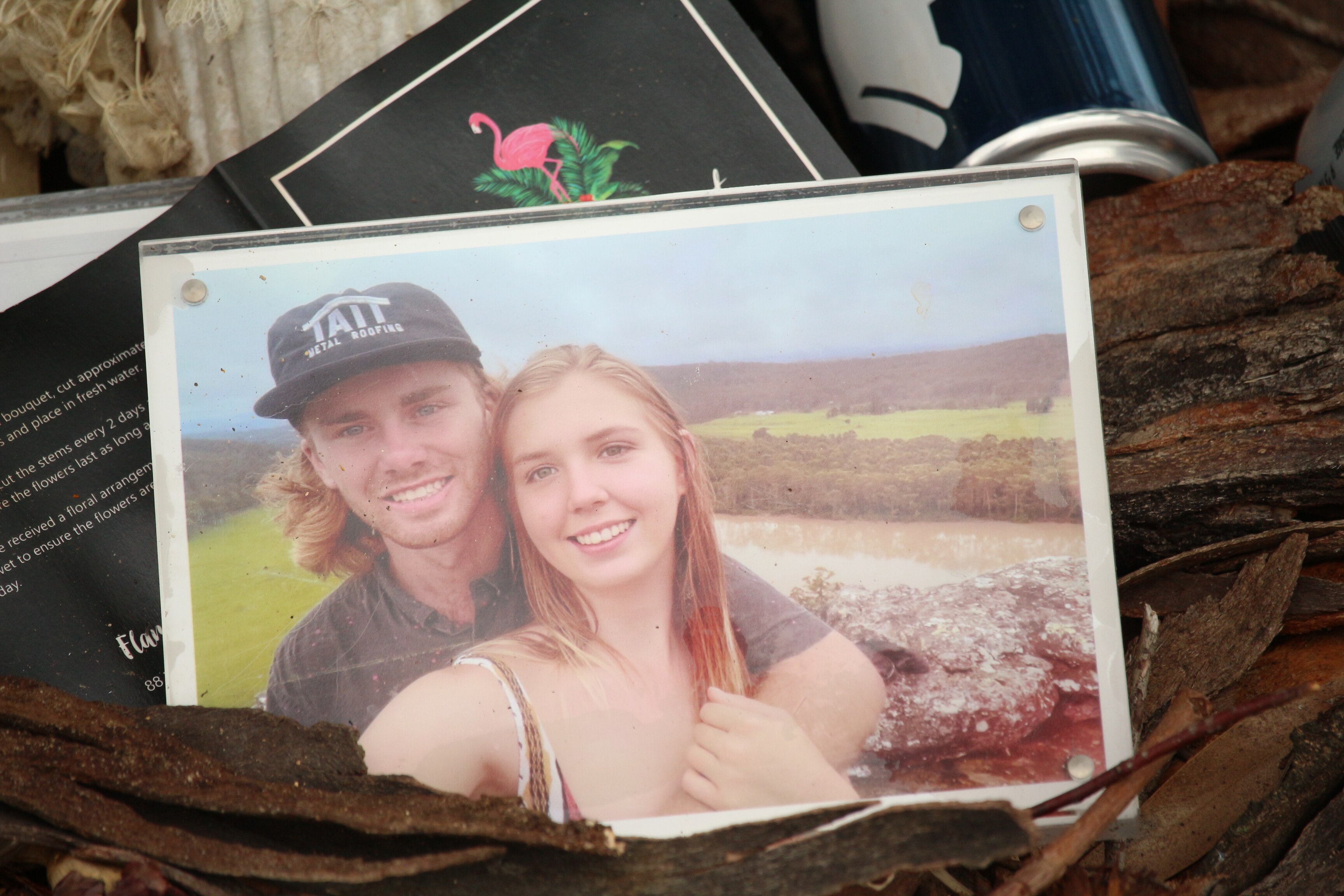 Una imagen enmarcada de un joven y una mujer abrazándose, dejada en el tronco de un árbol.