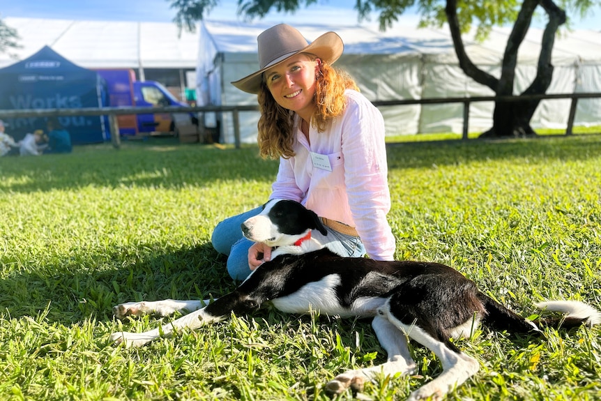A stock woman wearing a pink shirt, blue jeans and hat with a black and white border collie dog.