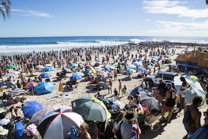 a huge crowd on the beach to watch a professional surfing contest