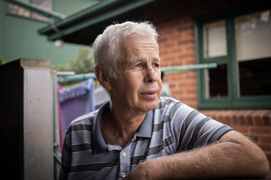 An older man looks out of the frame over a fence.