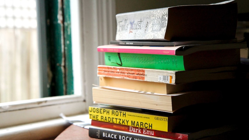 A pile of books, including Joseph Roth's The Radetzky March and A. S. Patrić's Black Rock White City, stand on a side table.