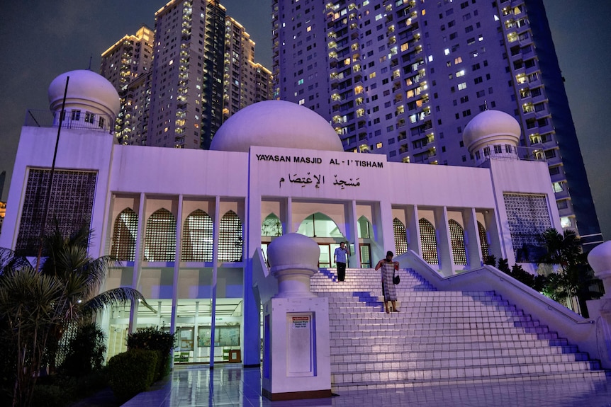A white mosque with an apartment building in the background, at night.