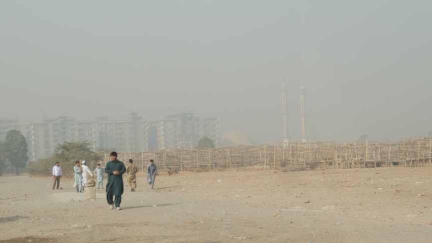 A group of boys play cricket on a barren piece of land.