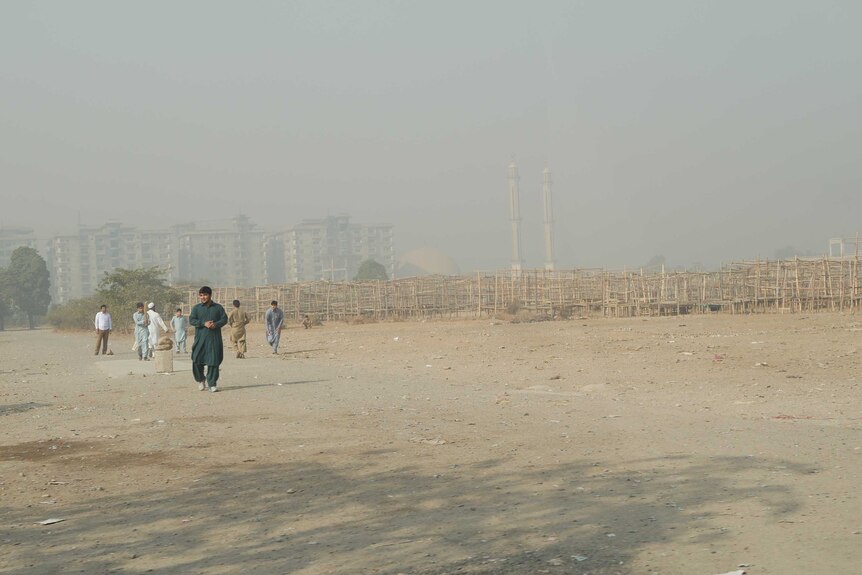 A group of boys play cricket on a barren piece of land.