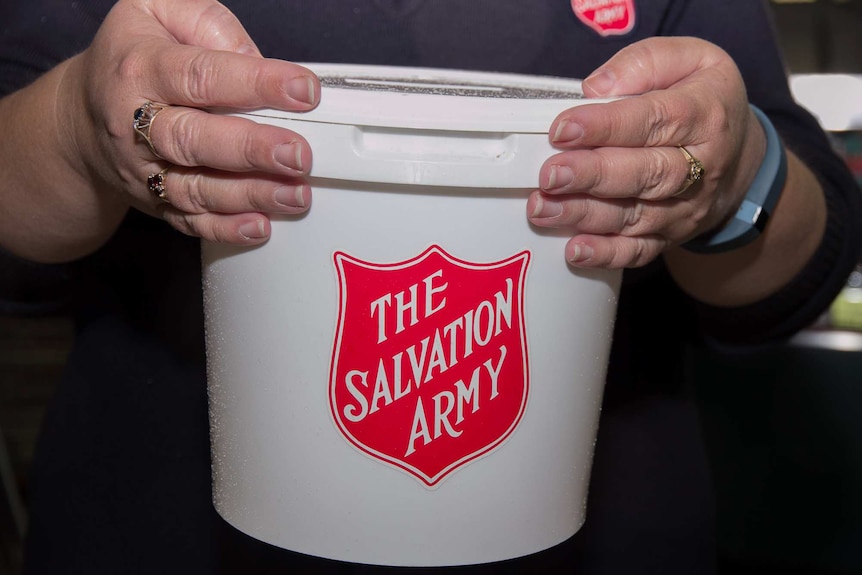 Close up of a woman's hands holding a white bucket with The Salvation Army written in red on it.