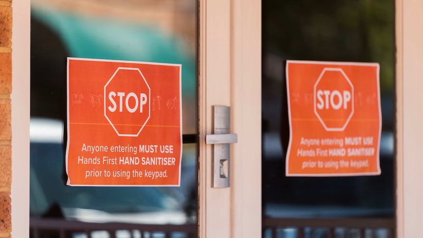 Two signs hang in the windows of a door instructing people to sanitise their hands.