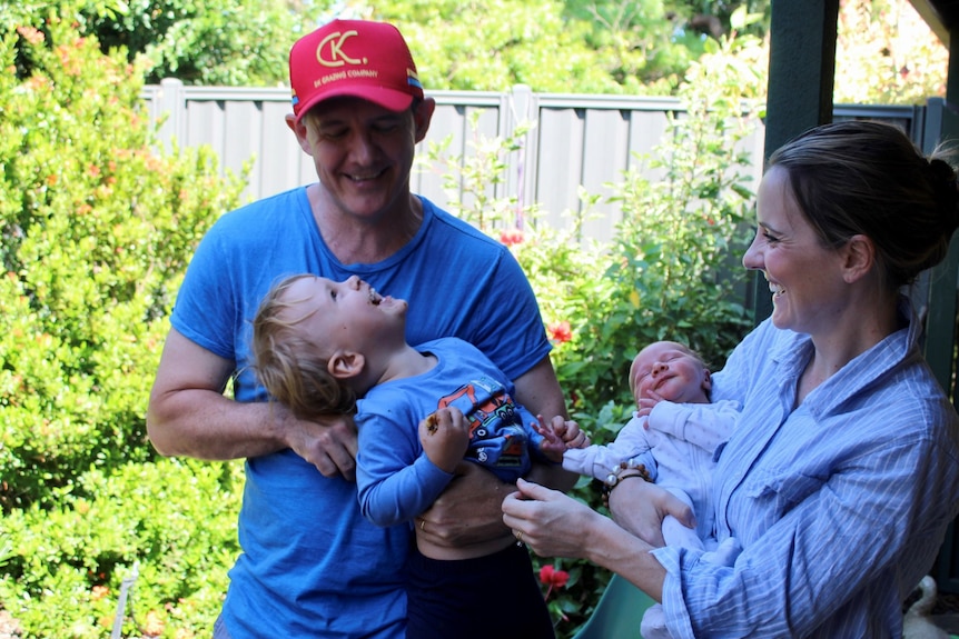 A happy man and his wife play with two young boys in the backyard.