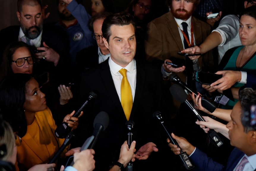 Matt Gaetz speaking while surrounded by reporters holding microphones