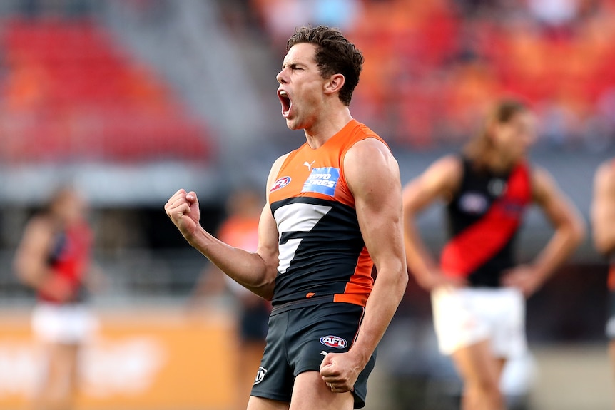 An AFL player closes his eyes, pumps his fists and roars in celebration after kicking a goal.