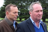 Tony Abbott and Barnaby Joyce on a dairy farm. Both men have stern expressions on their faces