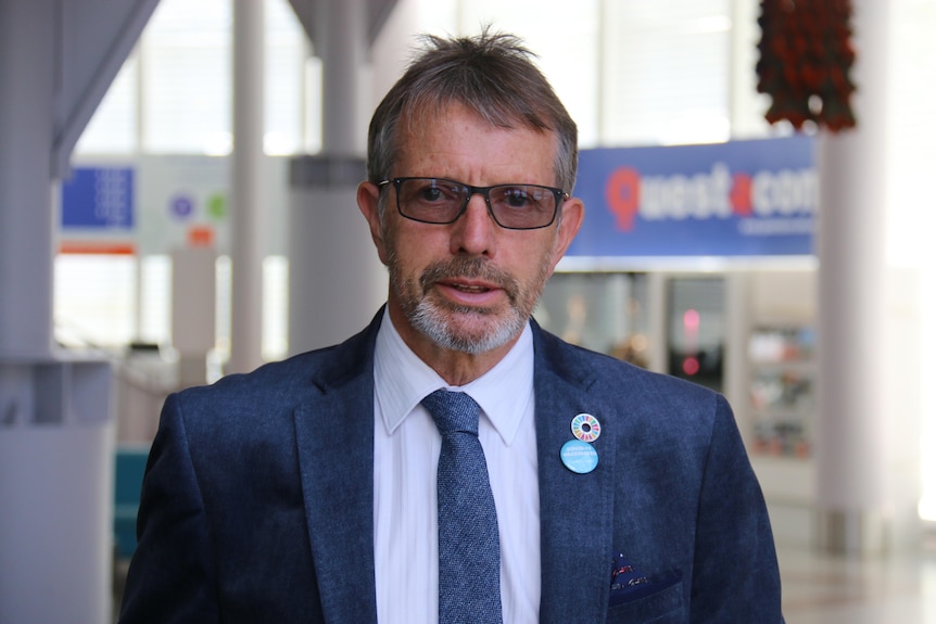 A man wearing a glasses a navy suit 