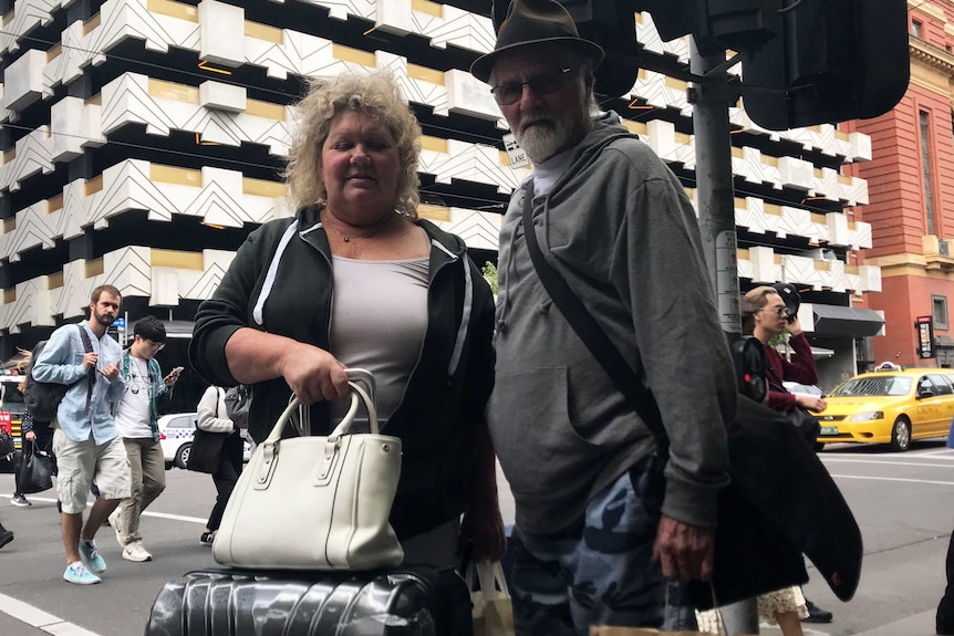 Caroline and Cam Edman standing outside an apartment building with their luggage.