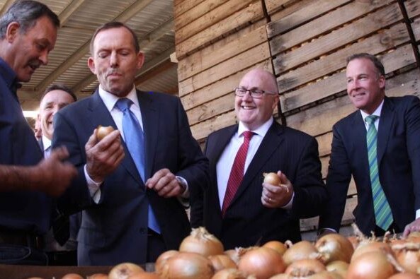 Man in a suit eats a raw onion with the skin on surrounded by other men in suits 