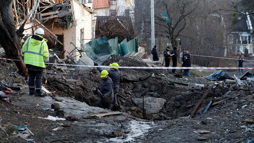 People work at a site of a Russian missile strike that left a crater in the middle of a path.