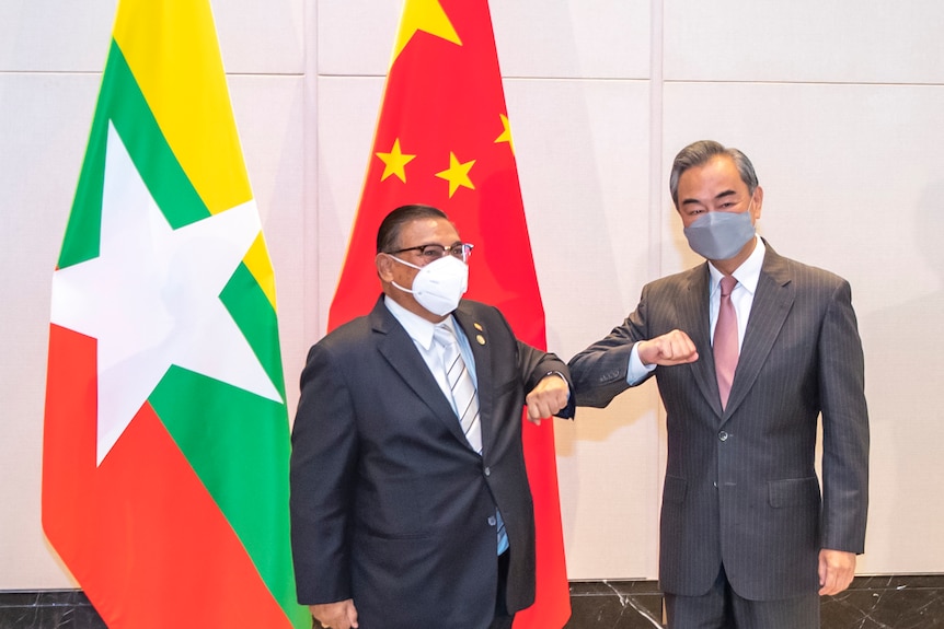 Two men bump right elbows in front of a Myanmar flag and a Chinese flag