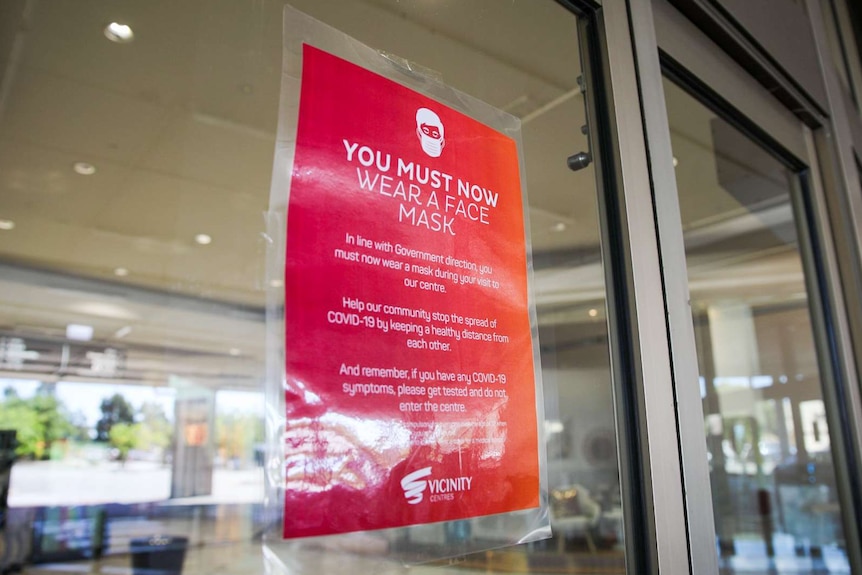 A red sign at a shopping centre telling people they must wear a face mask.