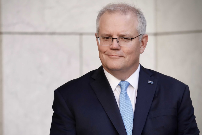 Scott Morrison stands in a courtyard with a wry smile on his face.