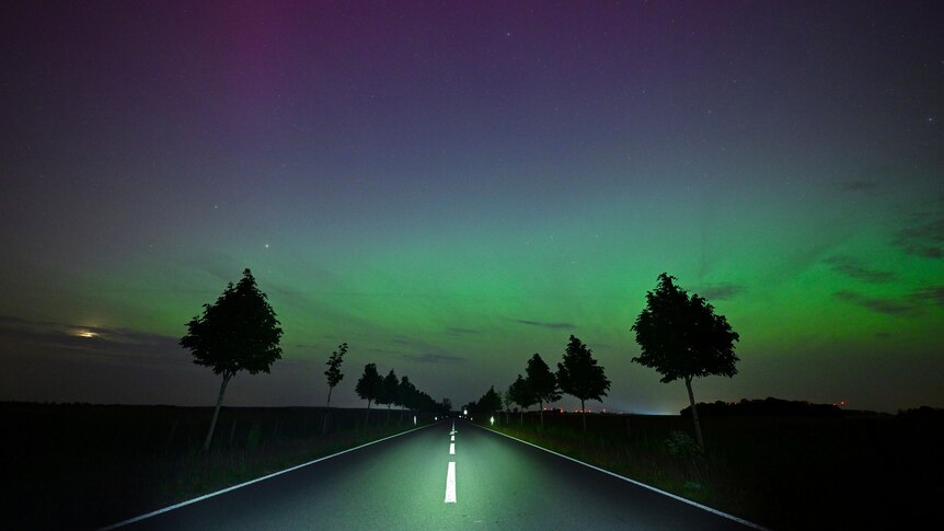 An empty road way wiht the sky lit up in green late at night
