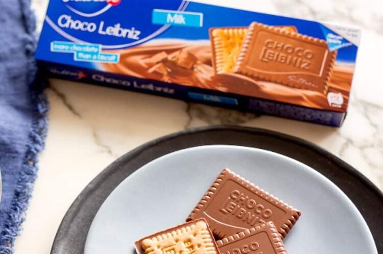 Some Choco Leibniz biscuits are seen from above sitting on a plate next to their packaging and a mug of coffee