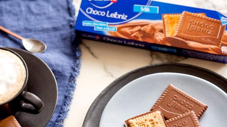 Some Choco Leibniz biscuits are seen from above sitting on a plate next to their packaging and a mug of coffee