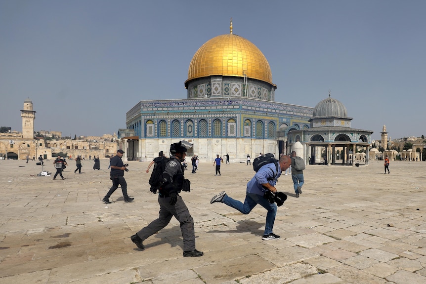 A member of Israeli police runs after a cameraman during clashes with Palestinians at the compound that houses Al-Aqsa Mosque.