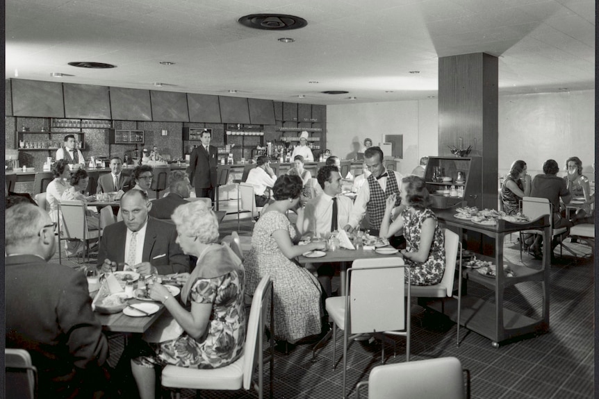 A black and white picture of a busy motel dining room in 1962, staff can be seen waiting on tables and serving.