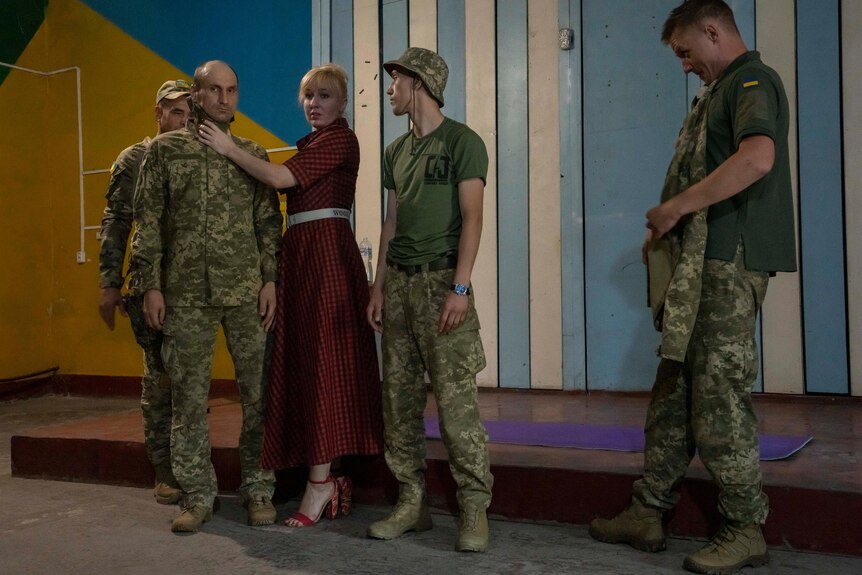 Medic Nataliia Voronkova stands among soldiers giving medical training, her hands are placed around one soldier's neck.