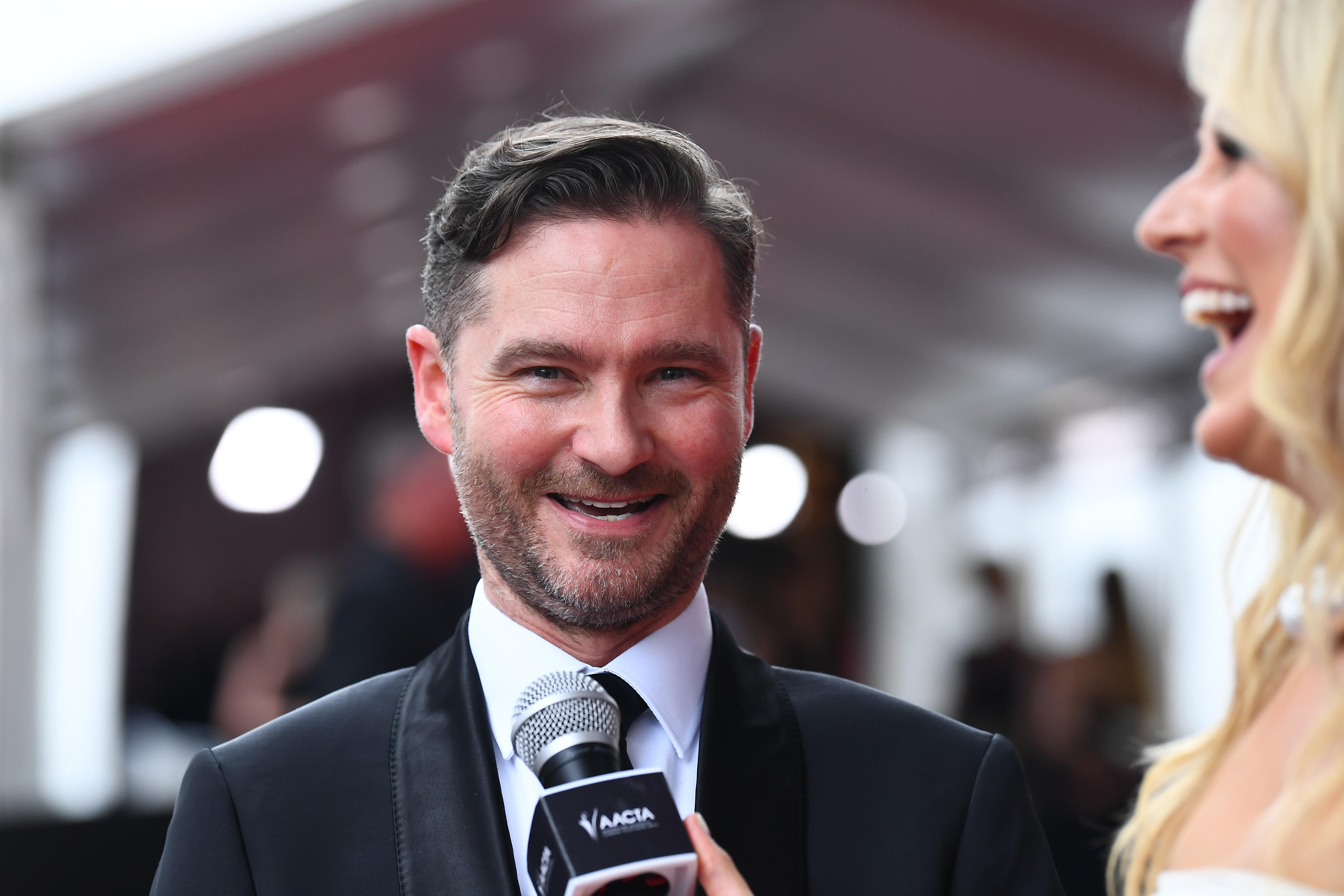 A man in a suit laughing with a lady next to him laughing with a microphone