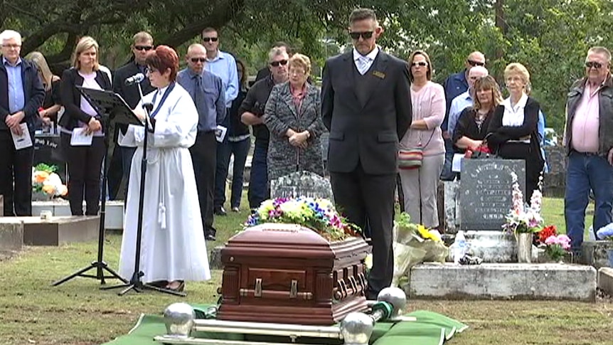 Mourners gather around the coffin of David Routledge, at a cemetery