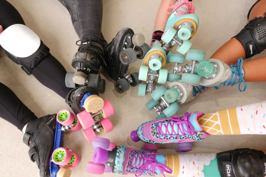 Five pairs of feet wearing skates in a circle on the ground.