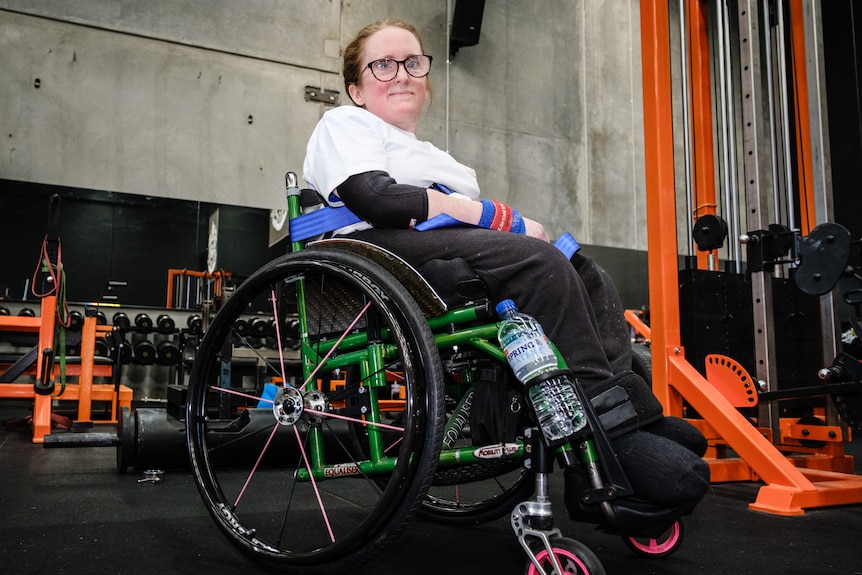 Ainslee Hooper sits in her wheelchair in a gym and smiles.