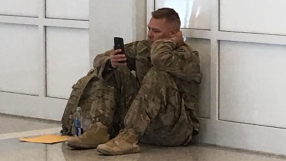 Soldier sits against wall, glued to his phone.