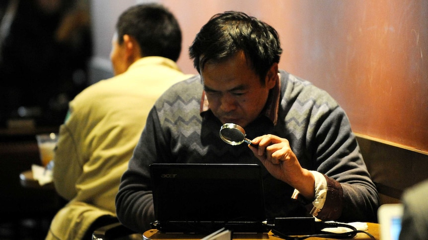 A Chinese man peers at his laptop while in an internet cafe