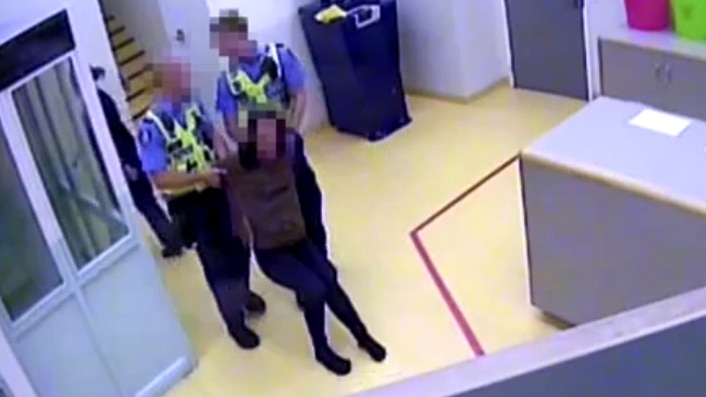 A CCTV picture of two police dragging a woman across a police station room.