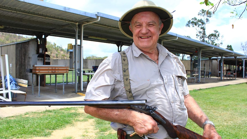 Les Bennell holds an old rifle while wearing a safari hat and braces decorated with African wildlife.