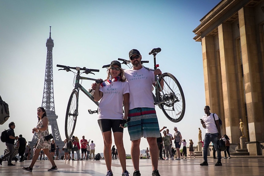 Terror victim's parents stand in front of Eiffel Tower with their bicycles.