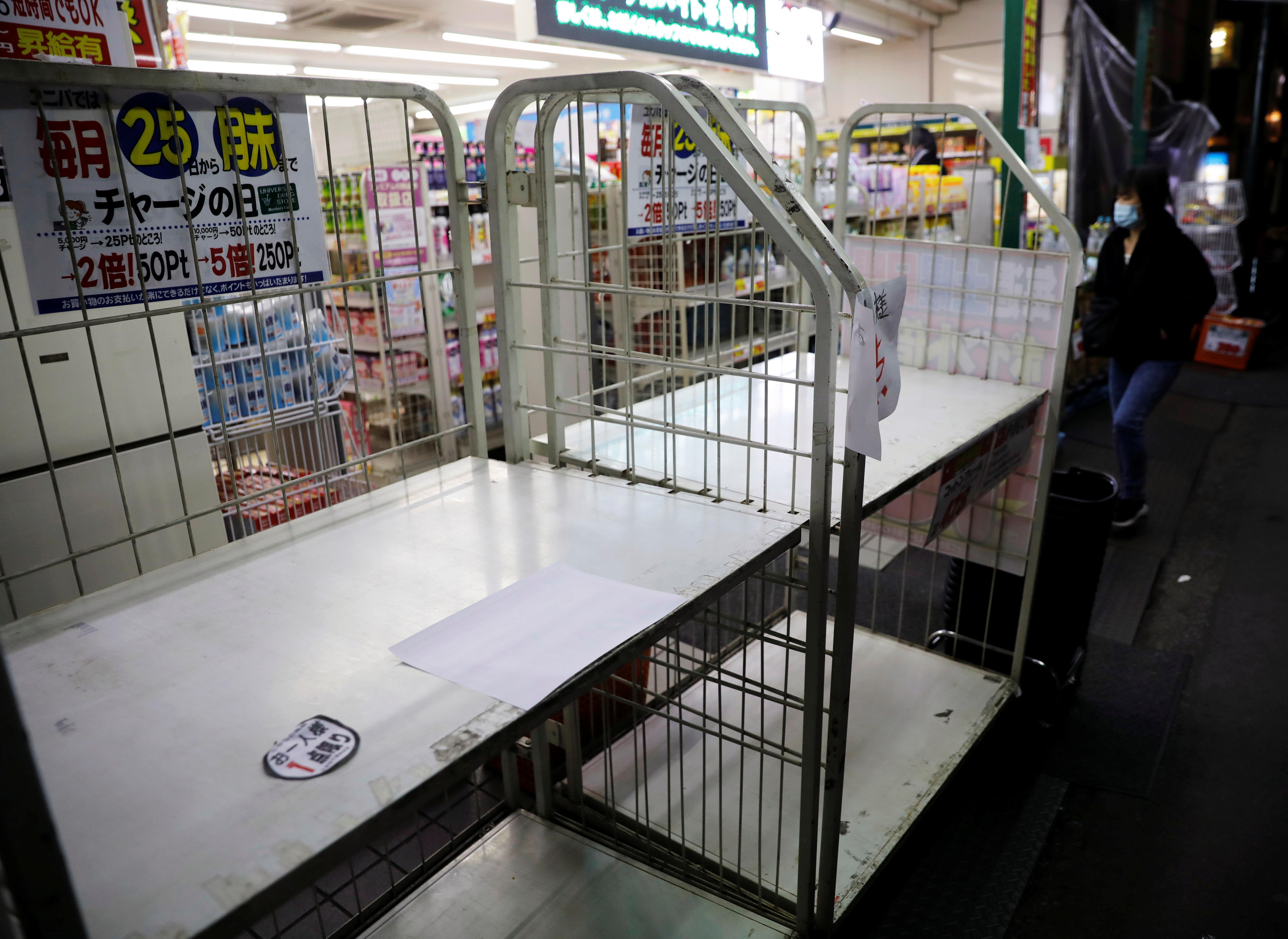 A person wearing face mask walks into a shop of empty shelves.