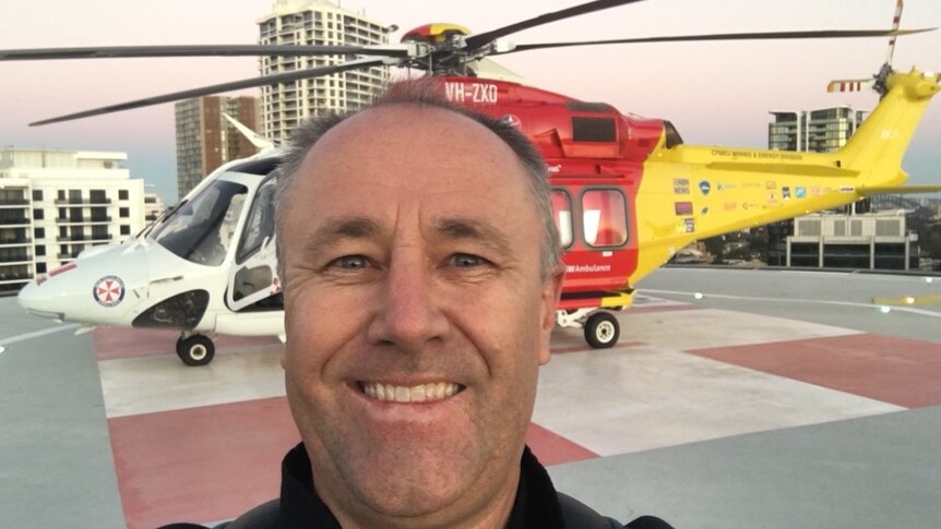 Man smiles in front of the red and yellow rescue helicopter