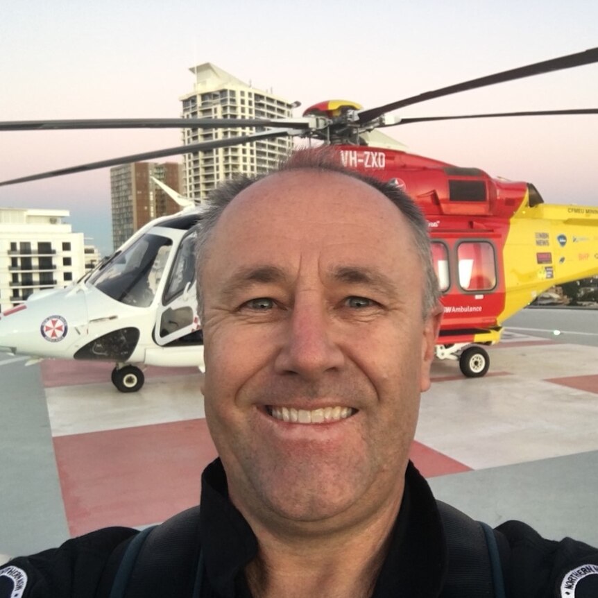 Man smiles in front of the red and yellow rescue helicopter