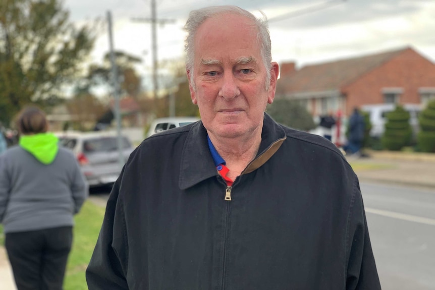 A man with grey hair a dark jacket standing on a suburban street.