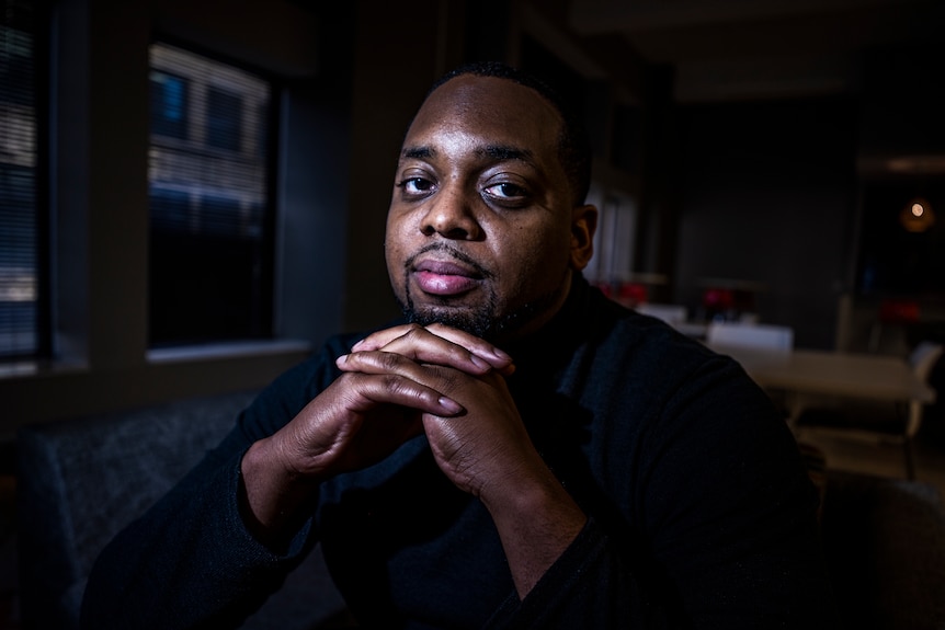 Brandon Mitchell poses for a picture as he sits with his hands folded under his chin.