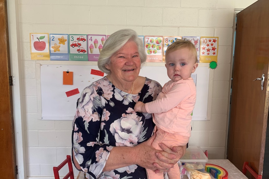 a happy grandmother holds a cute baby wearing pink.