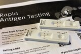 Two negative RAT tests sit on instruction paper