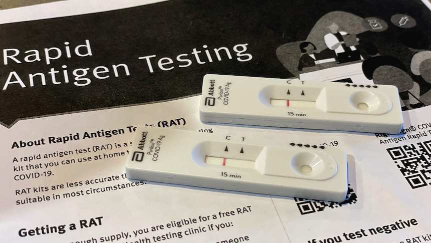 Two negative RAT tests sit on instruction paper