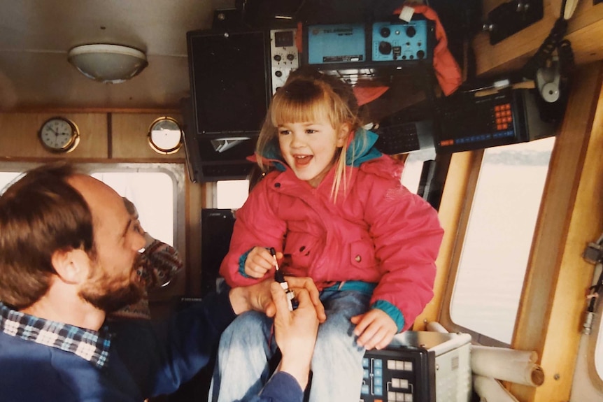 Naomi Wisby as a child in the cabin of a boat with her father.