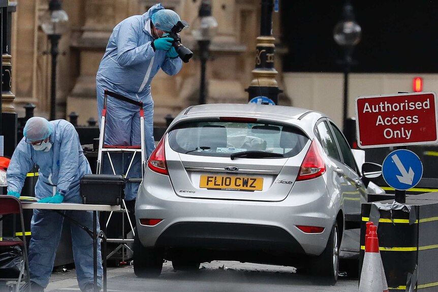 Officials in protective blue suits inspect car that crashed into UK parliament barriers