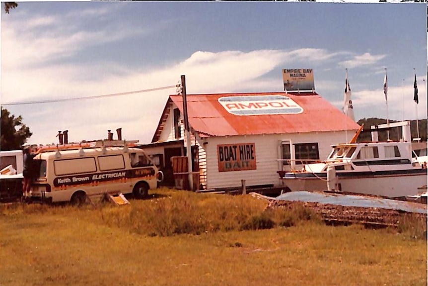 A colour photograph of a boatshed with red roof with ampol written on it, with a van parked beside it.
