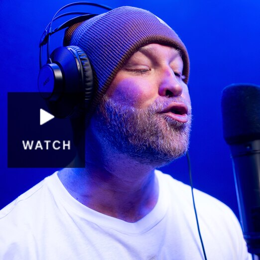Person wearing a beanie with headphones on in front of a microphone